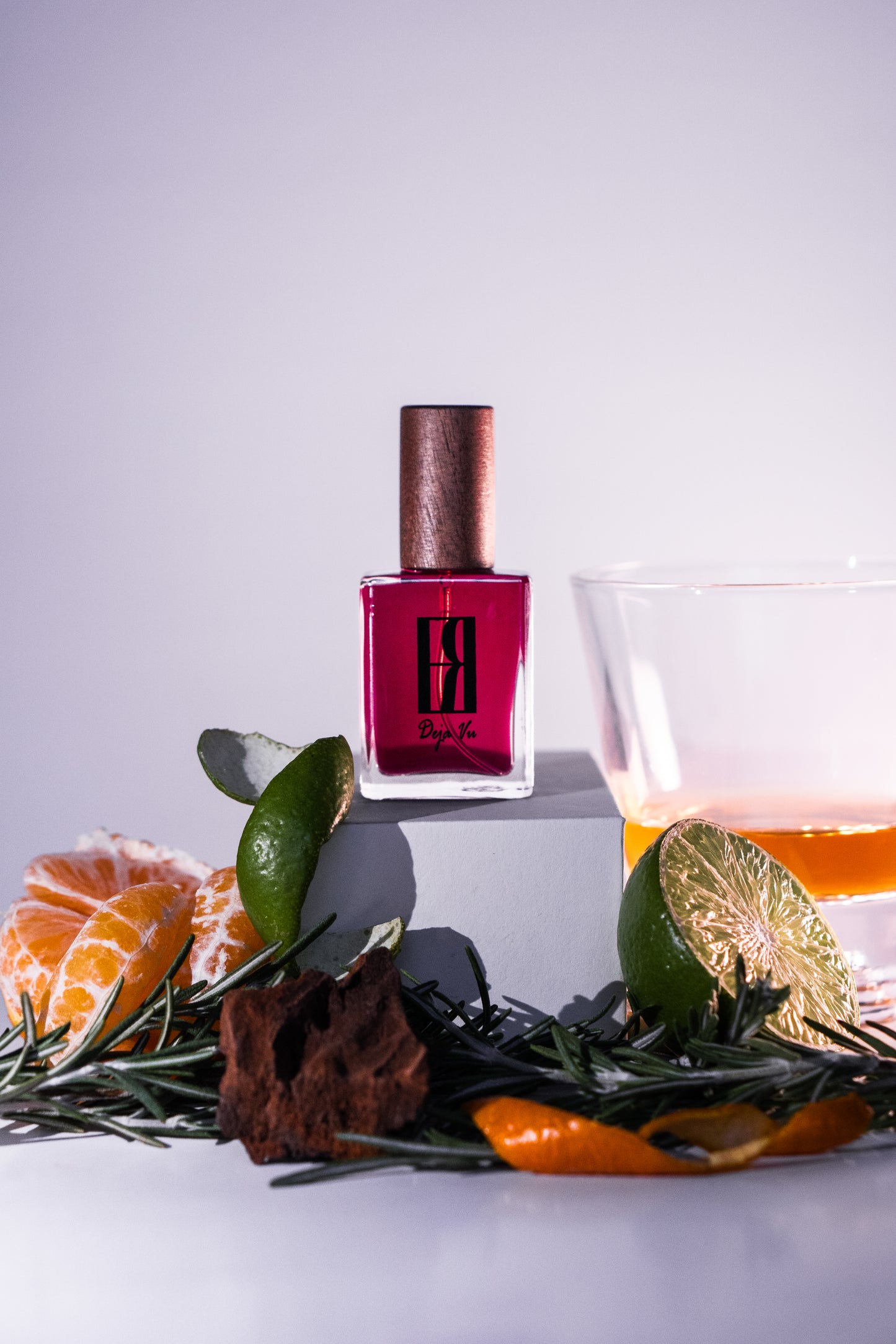 Perfume bottle with orange, cedarwood, cognac and rosemary leaves on a light background