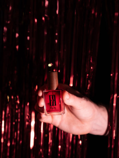 Hand holding an Elysian Ramaro Midnight Celebration perfume bottle coming through a red shiny curtain